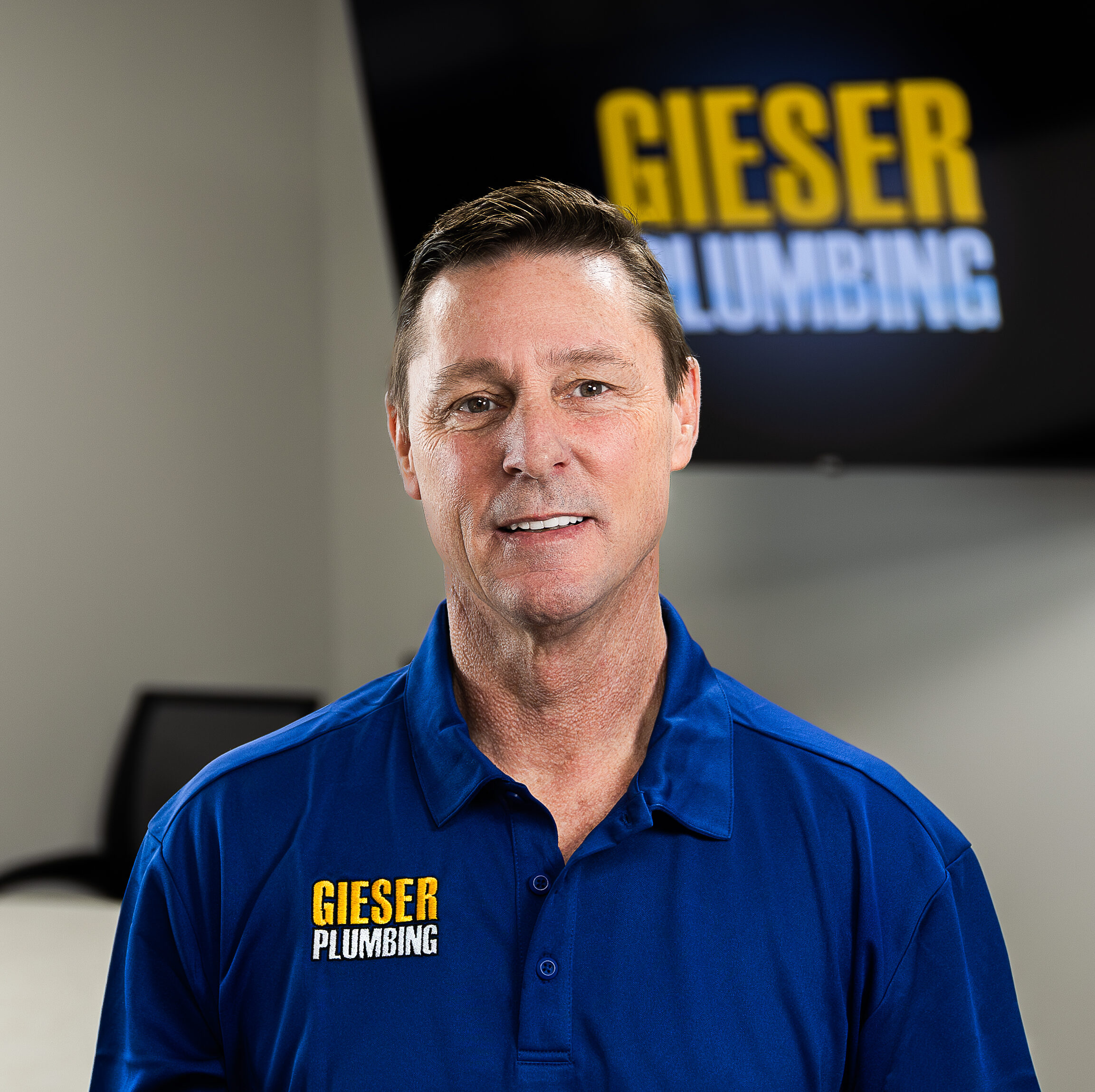 Close-up of a man in a blue polo with the 'GIESER PLUMBING' logo on his chest.